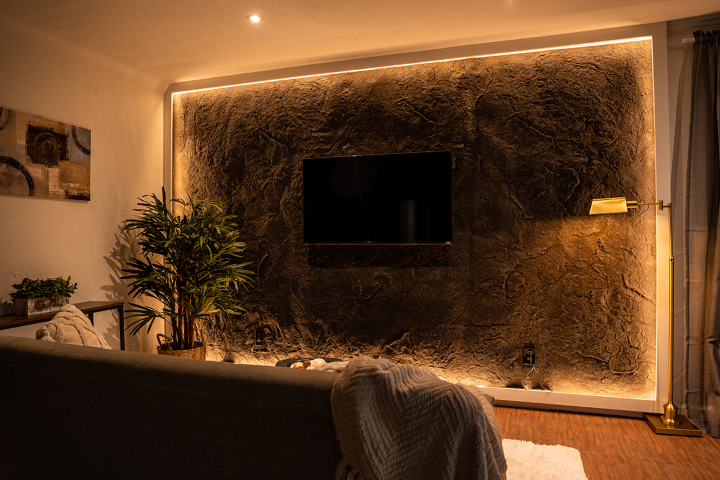 A Dragonstone Panel is mounted to a wall, with the edge illuminated by LEDS. In front, a tv is mounted