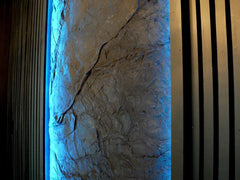 Interior Accent Wall covered by Slate Wall Panel. Black Wood Slats and Blue Light enjoin each Side of Panel